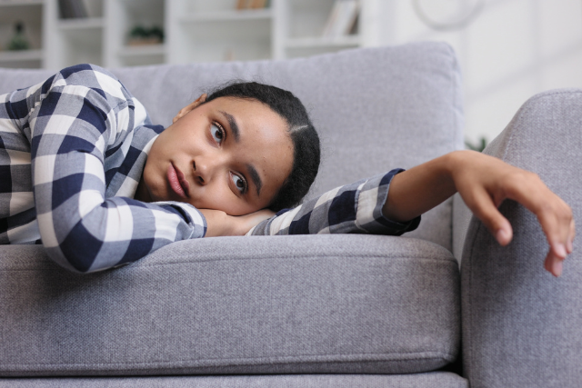 浮かない顔でソファに寝転んでいる女性