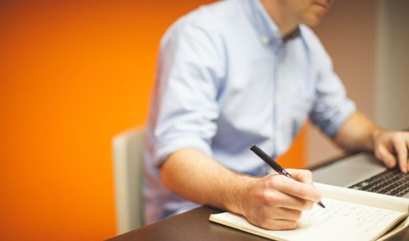 パソコンを操作しながらメモをとっている男性