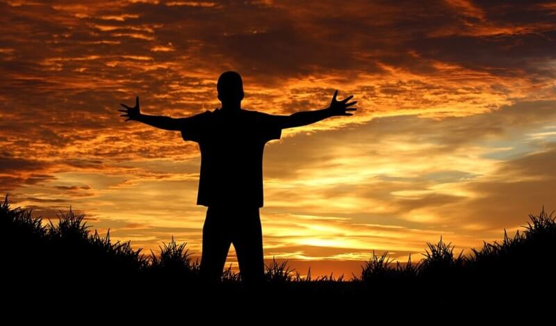 夕日に向かって両手を広げる男性