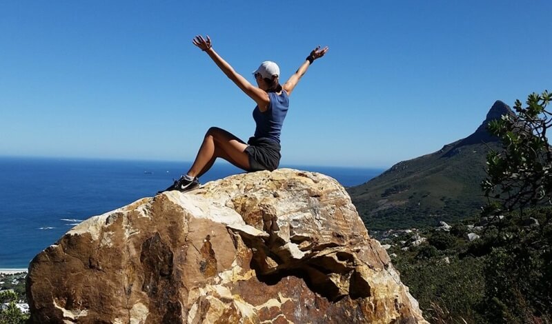 両手を広げて岩の上に座っている女性が