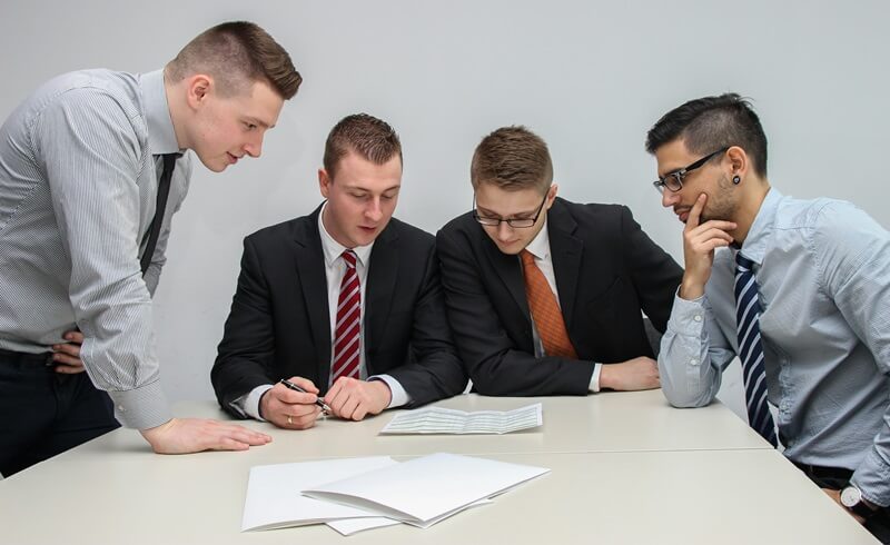 資料を見ながら考えているスーツの男性4人