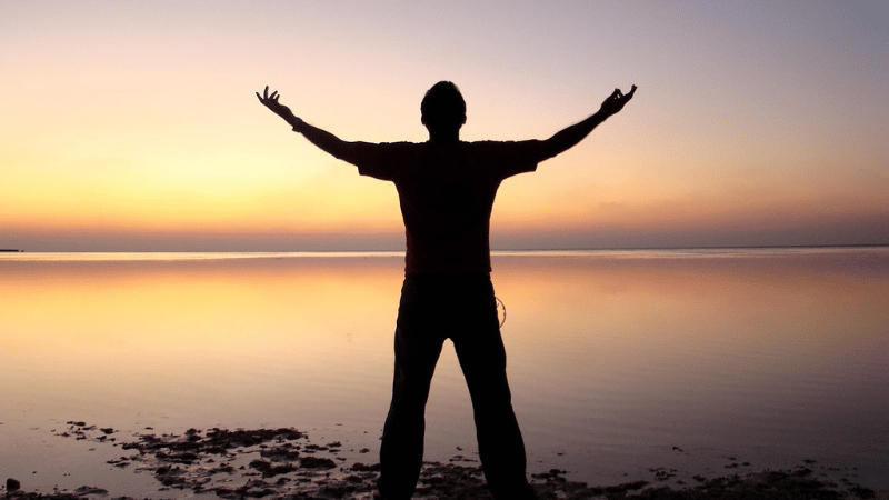 夕日の前で両手を広げる男性