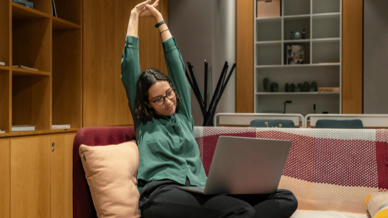 ノートパソコンを膝に乗せて伸びをする女性