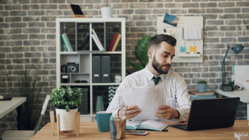 書類を手にしながらパソコンを見る男性