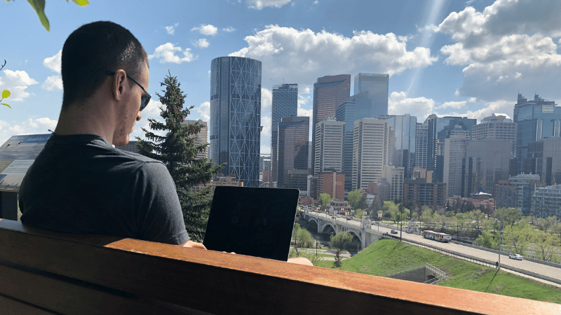 屋外のベンチに座ってパソコンを開いている男性