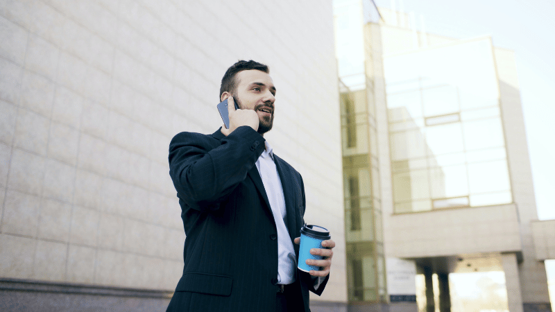 屋外でコーヒー片手に笑顔で電話している男性