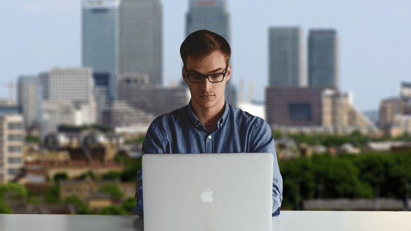 オフィス街を背景にパソコンを開く男性